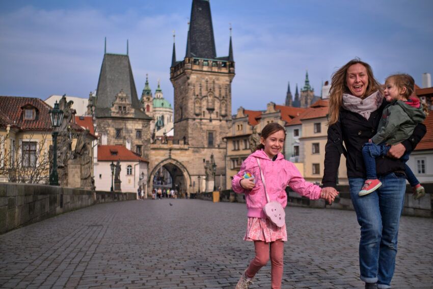 A mom and two kids walking on Charles Bridge with old Town in the background.