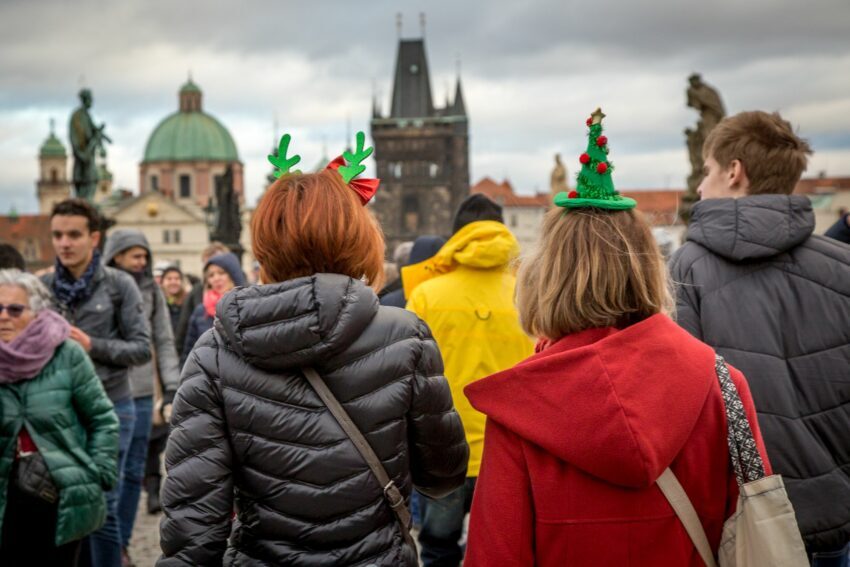 People walking ahead of the photographer on Charles Bridge with Christmas tree hats, Prague, Czech Republic