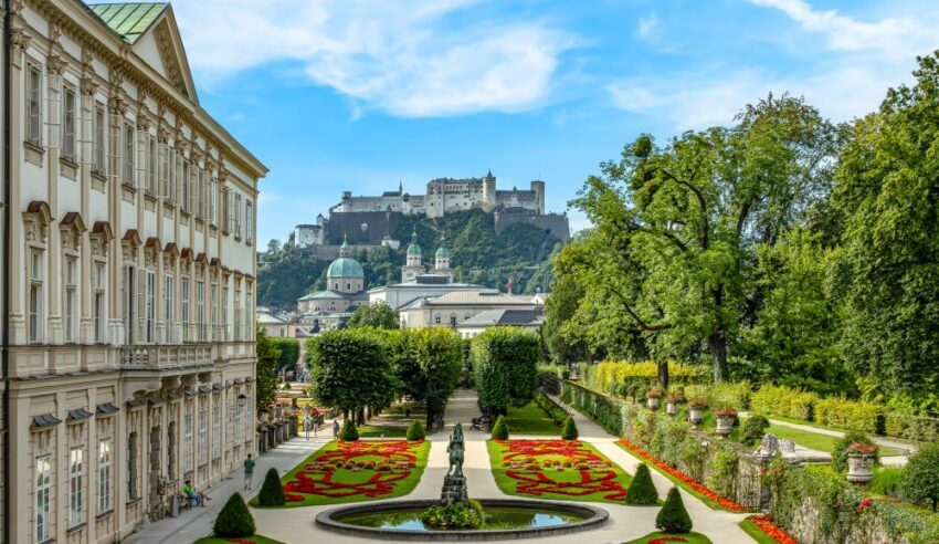 View of Mirabell Gardens in Salzburg, Austria, with Hohensalzburg Fortress in the background, against a backdrop of a bright blue sky