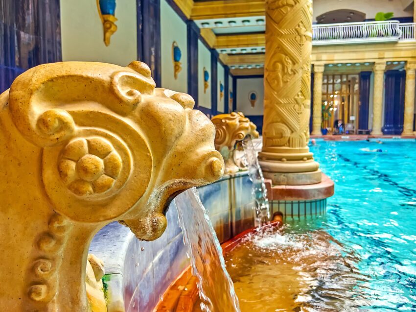 Golden lions spouting water into a pool at Gallert Baths in Budapest, with matching golden columns behind them